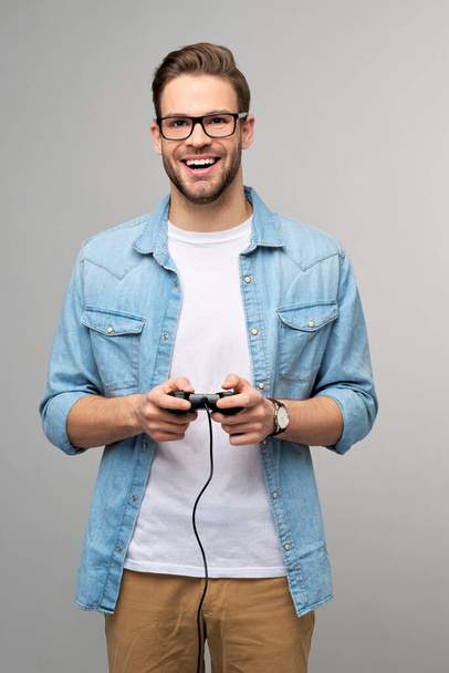 young man in casual jeans shirt holding joystick or gamepad playing game - Фото, изображение