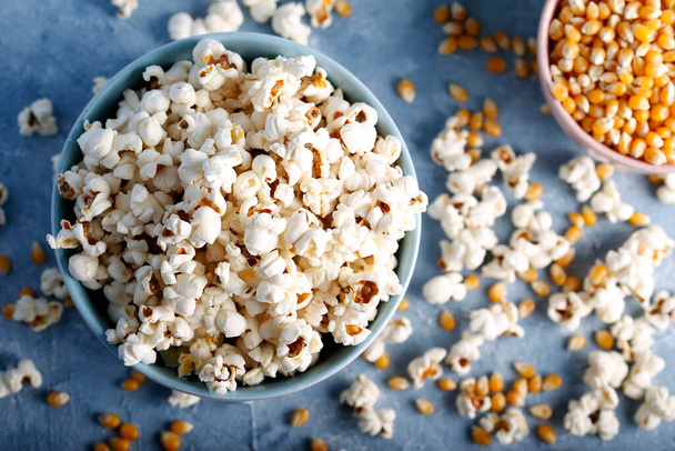 Salziges Popcorn in einer blauen Schüssel mit Maiskolben auf blauem Hintergrund. - Foto, Bild