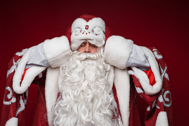 Santa Claus get tired and grabbed head for a headache, closed eyes, studio portrait on red background - Photo, Image