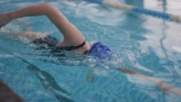 Langzame tracking van de vrouw in badpak, pet en bril zwemmen met borsten in het zwembad - Video