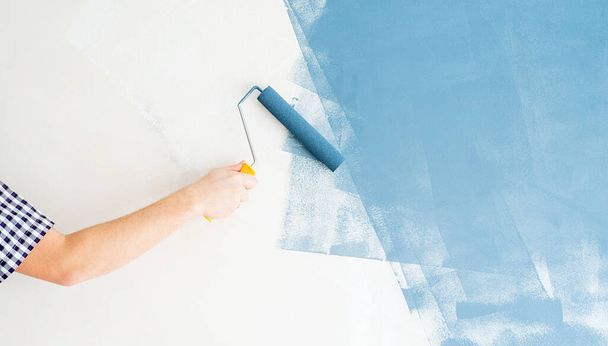 Reparatur und Verbesserung der Wohnung. Mann färbt Wand mit Walze blau - Foto, Bild