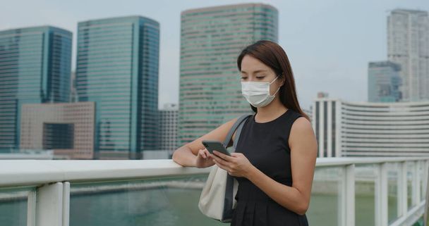 Kobieta nosić maskę twarzy i korzystania ze smartfona w mieście - Zdjęcie, obraz