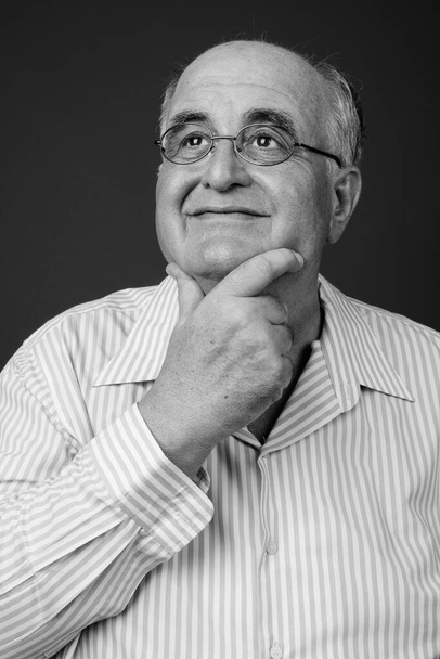 Studio shot of overweight senior man wearing eyeglasses against brown background - Foto, afbeelding