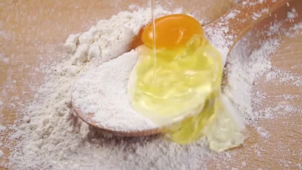 Raw egg falls into a pile of white flour in a wooden spoon. Egg yolk and white are spilled close up. Slow motion - Кадры, видео