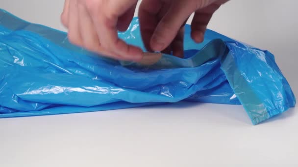 Ο άνθρωπος ανοίγει μια νέα πλαστική μπλε σακούλα σκουπιδιών κοντά σε ένα λευκό φόντο. - Πλάνα, βίντεο