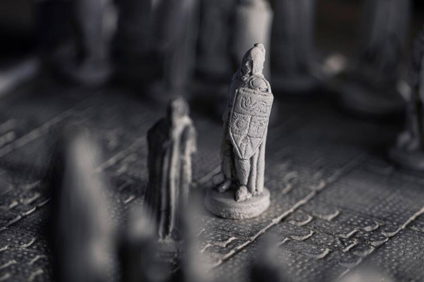 Stratejik bir satranç oyununun başlangıcında birbirine bakan iki piyonun portresi. Düello taş bir satranç tahtasında, taş heykeller de satranç taşları gibi dövüşecek.. - Fotoğraf, Görsel