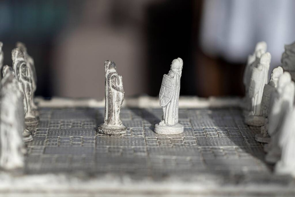 Ein Porträt von zwei Bauern, die sich zu Beginn einer strategischen Schachpartie gegenüberstehen. Das Duell wird auf einem Steinschachbrett mit Steinskulpturen als Schachfiguren ausgetragen.. - Foto, Bild