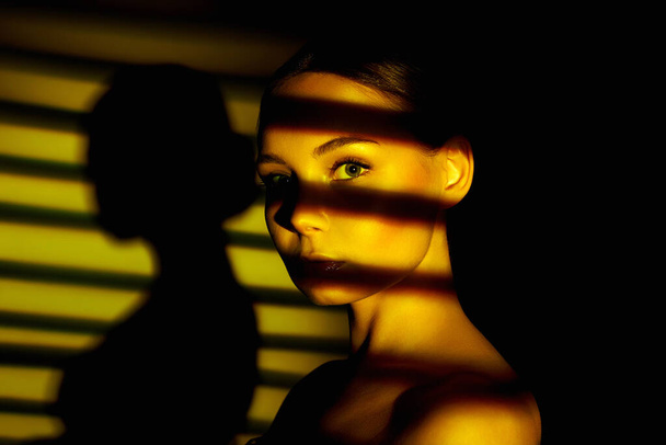 luce del tramonto che cade attraverso le tende sul volto della bella ragazza. sensuale giovane donna in ombra - Foto, immagini