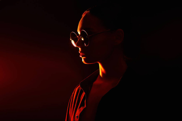 Gyönyörű fiatal nő napszemüvegben. Divatos hölgy piros lámpában. - Fotó, kép