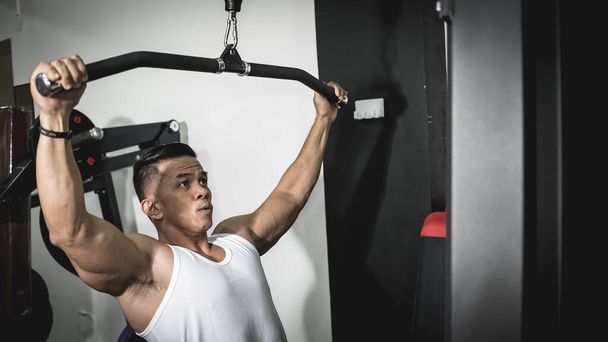 Un homme asiatique coupe propre et en forme faisant des pulldown lat à la salle de gym. Entraînement, entraînement des muscles du dos. - Photo, image