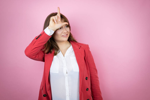 Jonge zakenvrouw over geïsoleerde roze achtergrond lachen van mensen met vingers op het voorhoofd doen verliezer gebaar bespotten en beledigend. - Foto, afbeelding