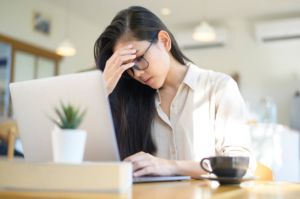 Een vermoeide en gestresste zakenvrouw met hoofdpijn van het gebruik van laptop in de coffeeshop - Foto, afbeelding