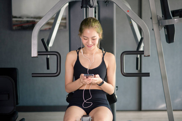 A beautiful smiling woman in earphones using a social network and listening to music at gym, Fitness and technology concept - 写真・画像