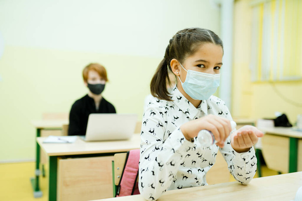 A girl sits in a class at a lesson in a medical mask using an antispetic for hands - Photo, Image
