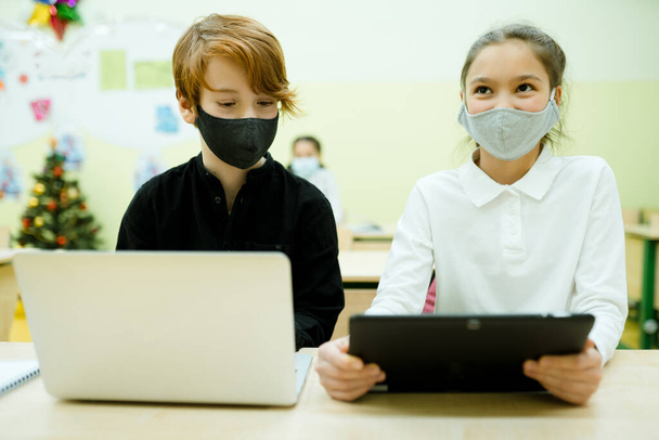 A girl and a boy during a pandemic study at school holding tablets in their hands - Foto, Imagen