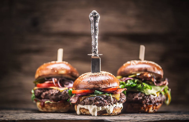 Assortment of three various burgers ready to be plated, with a dark wooden background. - Foto, immagini