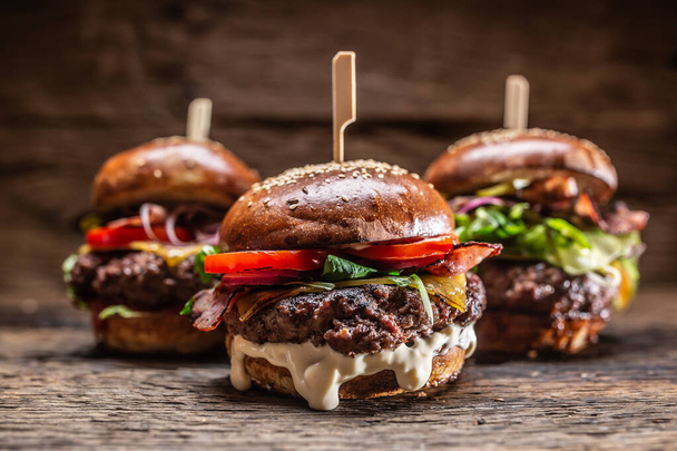 Assortment of three various burgers ready to be plated, with a dark wooden background. - Zdjęcie, obraz