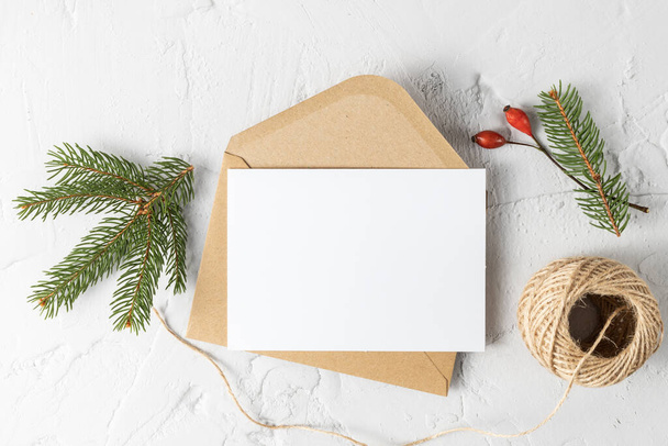 Χριστουγεννιάτικη κάρτα mockup με έλατο υποκατάστημα, λευκό χαρτί και διακόσμηση σε λευκό φόντο πέτρα. - Φωτογραφία, εικόνα