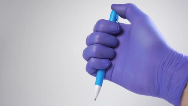Рука в медицинской перчатке нажимает кнопку пластиковой автоматической шариковой ручки на белом фоне. - Кадры, видео