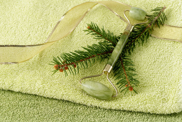 Jade rolo facial para anti-envelhecimento massagem da pele com ramo de abeto em uma toalha macia. Natal spa cartão de presente - Foto, Imagem