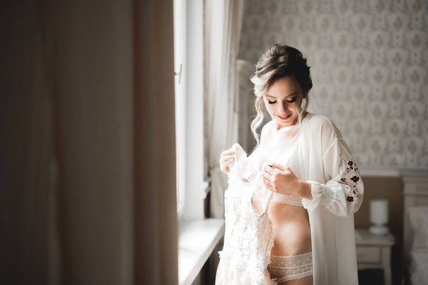 Krásná nevěsta nosí módní svatební šaty s peřím s luxusním make-up a účes, studio focení uvnitř - Fotografie, Obrázek