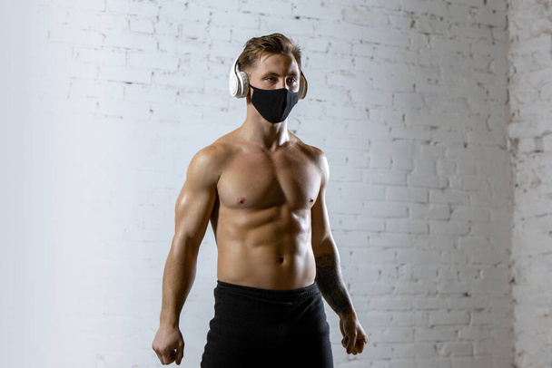 Professional male athlete training on brick wall background wearing face mask. Sport during quarantine - Foto, afbeelding