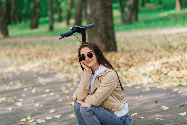 Young woman riding an electric scooter in autumn park. Green transport, traffic jam problems. - Photo, Image