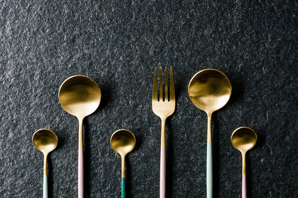 Set van elegante roze, groene en gouden lepels en vork op zwarte achtergrond Luxe en trendy gerechten. Platte bovenaanzicht. - Foto, afbeelding