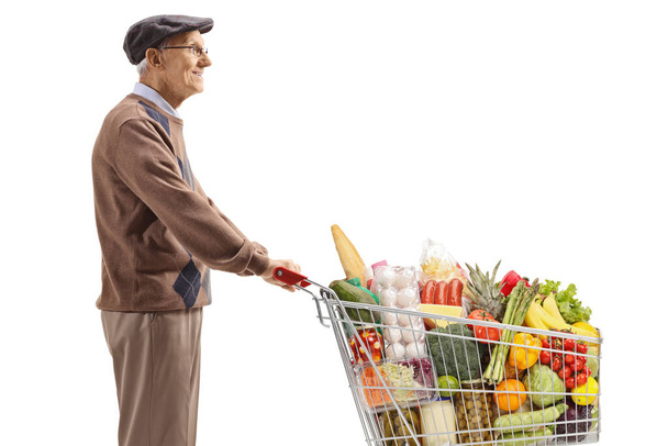 Pensioner standing and waiting with a shopping cart with food products isolated on white background - Φωτογραφία, εικόνα