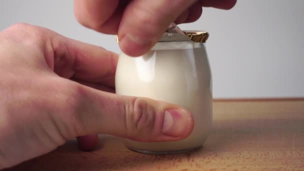 Ouvrez un pot en verre de yaourt naturel en enlevant le couvercle en feuille d'or. Sur une planche à découper en bois. Gros plan - Séquence, vidéo