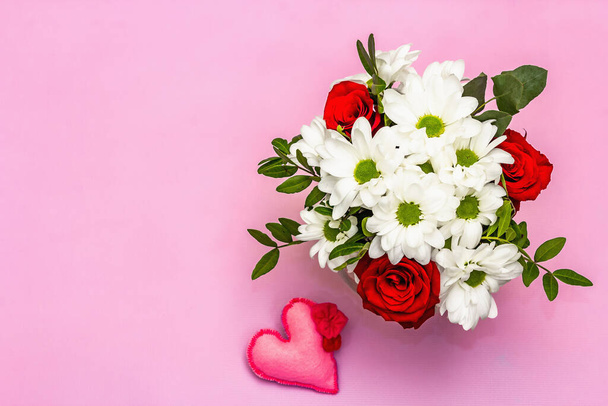 Egy csokor friss virág üvegvázában és lágy nemezszívben. Valentin-nap vagy esküvői koncepció. Gyengéd rózsaszín texturált háttér - Fotó, kép