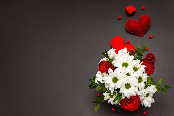 Ένα μπουκέτο από φρέσκα λουλούδια σε γυάλινο βάζο και καρδιές από μαλακή τσόχα. Ημέρα του Αγίου Βαλεντίνου ή έννοια του γάμου. Μαύρο φόντο από μπετόν - Φωτογραφία, εικόνα