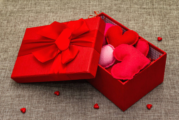Rote Geschenkschachtel mit handgemachten Filzherzen auf gewebtem Hintergrund. Valentinstag-Konzept - Foto, Bild