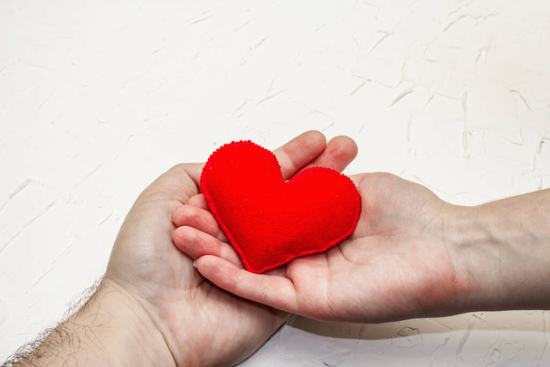 Концепция Дня Святого Валентина. Мужская и женская руки держат самодельное войлочное сердце. Белый патетический текстурированный фон - Фото, изображение