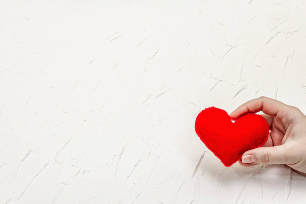 Koncept Valentýna. Ženská ruka drží domácí červené plstěné srdce. Bílé tmel texturované pozadí - Fotografie, Obrázek