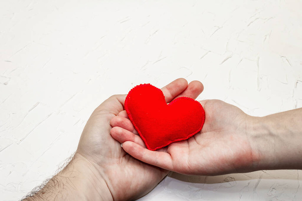Sevgililer Günü konsepti. Erkek ve kadın eli el yapımı bir keçeli kalp taşıyor. Beyaz macun desenli arkaplan - Fotoğraf, Görsel