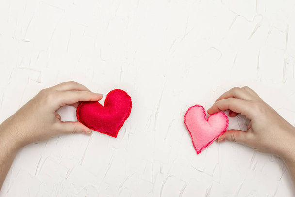 Concepto del Día de San Valentín. Las manos femeninas sostienen corazones de fieltro hechos en casa. Masilla blanca fondo texturizado - Foto, Imagen