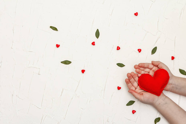 Concept de Saint-Valentin. Les mains des enfants tiennent un cœur en feutre fait maison. fond de mastic blanc - Photo, image