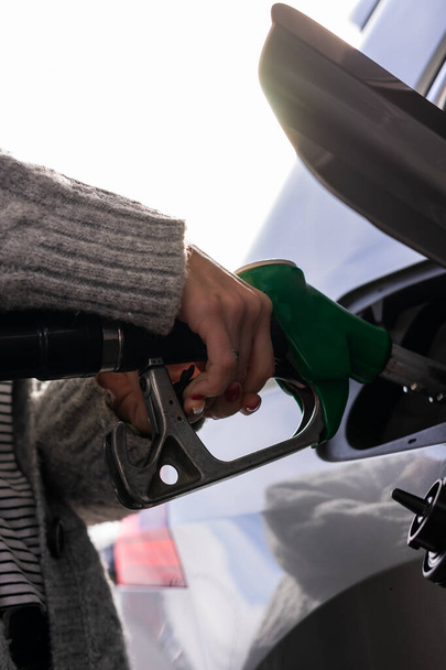 Eine junge Frau mit lackierten Nägeln und schönem Pullover füllt ihr Auto mit Benzin. Bild aus einem niedrigen Winkel aufgenommen. - Foto, Bild