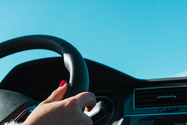 Una mujer con clavos pintados sostiene el volante de un vehículo. En el fondo, un cielo azul turquesa - Foto, Imagen