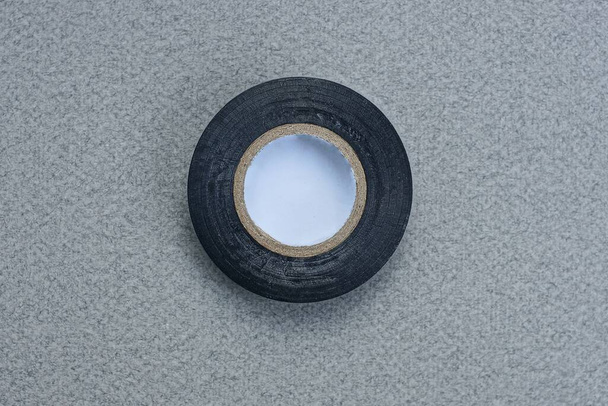 una madeja negra redonda de cinta adhesiva yace sobre una mesa gris - Foto, Imagen