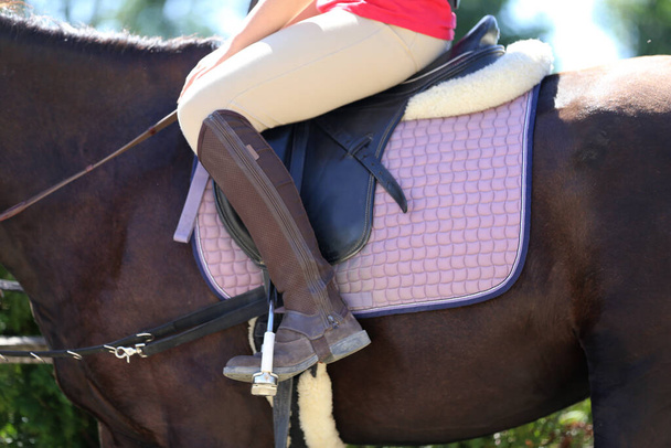 Old leather saddle with stirrups for show jumping race Saddle on a back of a sport horse. Equestrian sport event background - Photo, Image