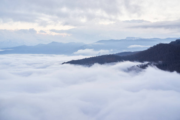 Belle vue panoramique irréelle sur les montagnes dans les nuages. Nuages bas, vue sur la forêt d'hiver et les montagnes depuis le pont d'observation, image horizontale d'un phénomène naturel étonnant. - Photo, image