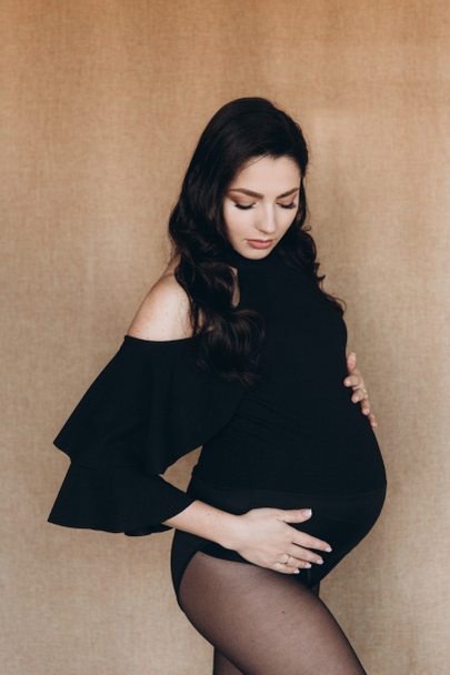 Pregnancy photo session in a photo studio with a fabric background in a black bodysuit and tights - Fotoğraf, Görsel