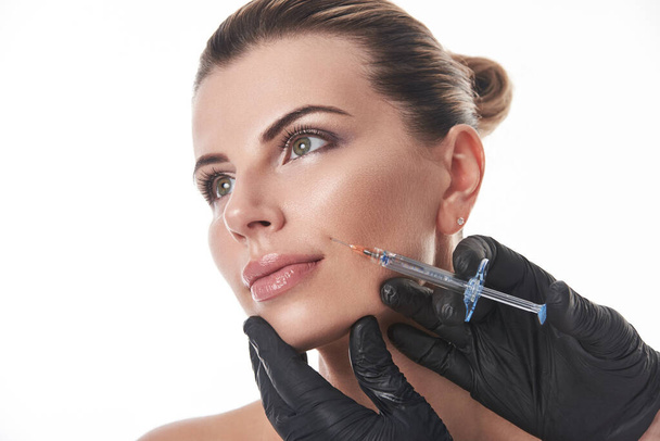 Uma jovem mulher branca bonita recebendo uma injeção em uma dobra nasolabial. - Foto, Imagem