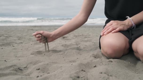 Žena na pláži padající černý písek z její ruky. - Záběry, video