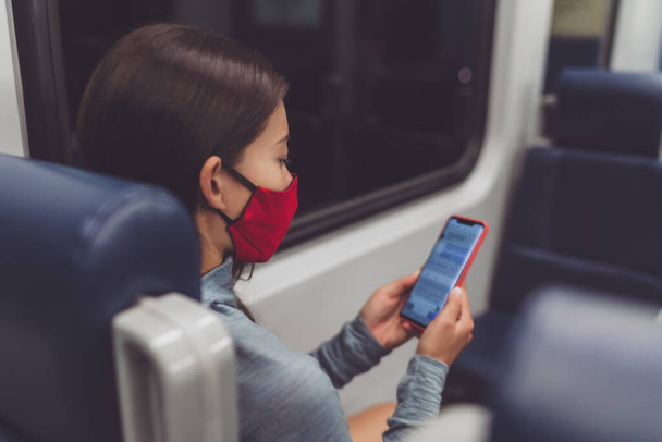 Train commute during corona virus pandemic. Woman passenger using mobile phone wearing face mask sitting in public transport texting online on contact tracing app - Φωτογραφία, εικόνα