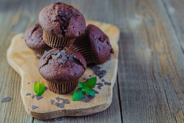 Muffins o cupcakes de chocolate recién hechos en casa sobre una tabla de madera sobre un fondo rústico de madera con hojas de menta verde fresca. Lugar para tu mensaje. Panadería, panadería - Foto, Imagen