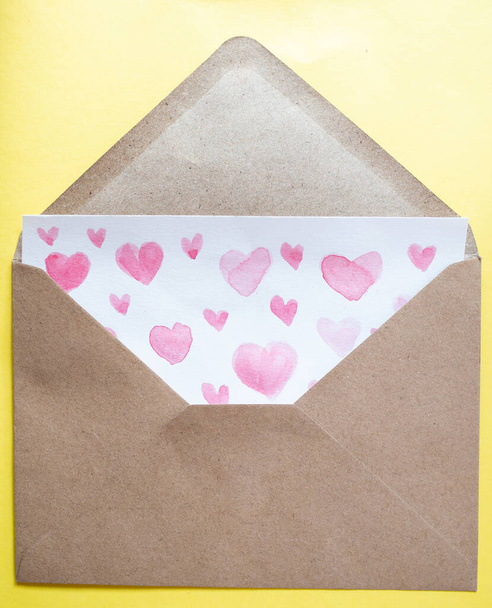 Love letter with water color pink hearts in a craft envelope on yellow background. - Foto, Imagen