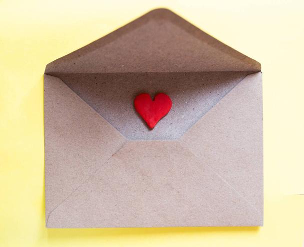 Love letter in a craft envelope with clay red heart on yellow background. - Photo, image